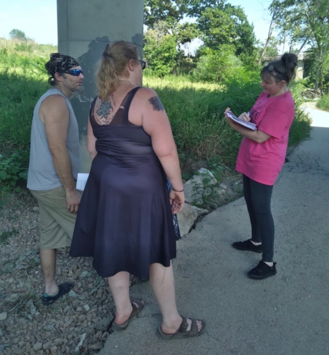 An outreach staff member taking notes while speaking with two people outdoors.